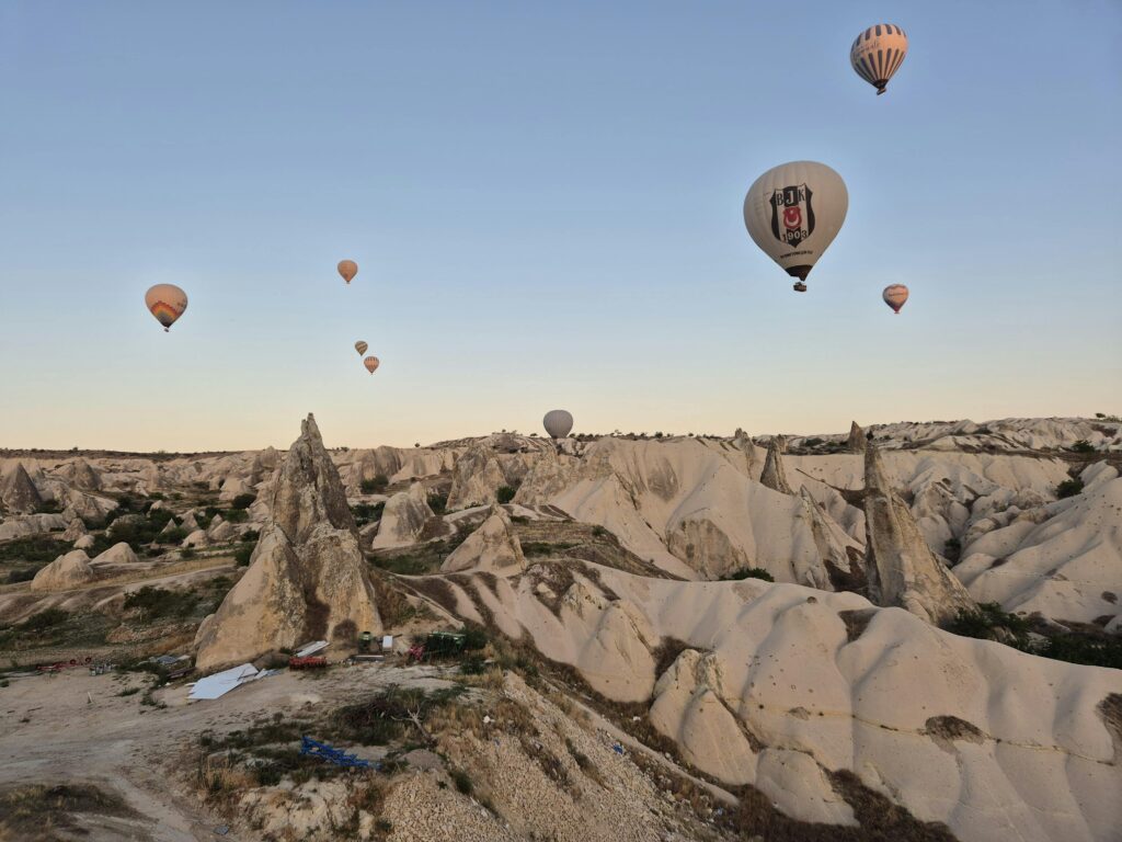 Aerial view of hot air balloons floating above the rocky formations of Cappadocia at sunrise.
