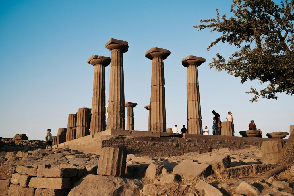 Ancient Greek temple ruins in Assos, Turkey at sunset, with visitors exploring the historic site.