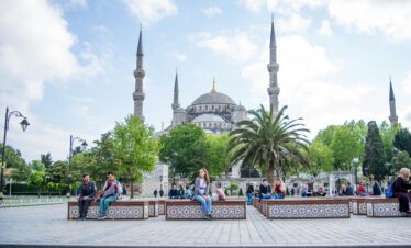 Daytime view of the Blue Mosque in Istanbul with people relaxing in the foreground. A blend of history and daily life.
